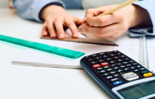 Närbild på miniräknare och elev som använder mätverktyg i kollegieblock