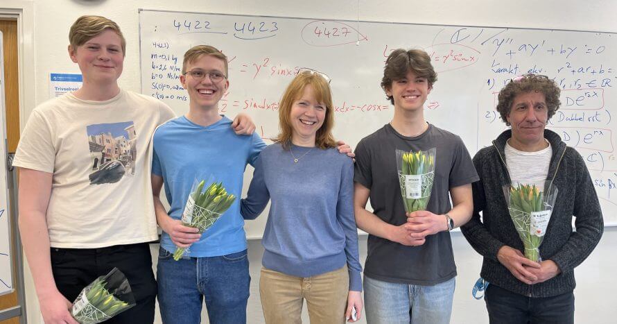 Tre elever står tillsammans med lärare och rektor och tar emot blommor