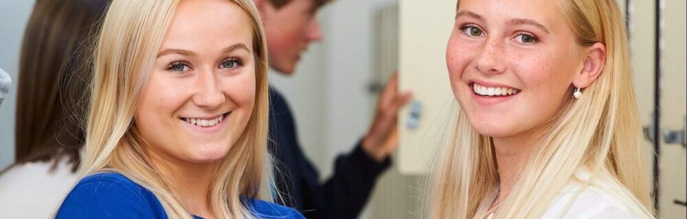 Två kvinnliga elever står framför skåp och håller i skolböcker